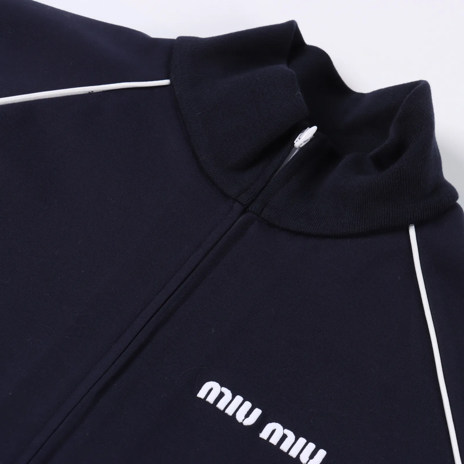 Miu Miu 24Fw Miu小標刺繡嵌線夾克外套                定織定染尼龍混紡棉布，棉纖維的加入提高了面料的透氣性和吸濕性，穿著更加舒適，具有良好的彈性，能夠迅速恢復原狀，不易變形，螺紋針織衣領，螺紋針織袖口和低邊，嵌線袋做工複雜，要將嵌條布對折並熨燙，然後按照牛皮紙實樣車半棉，車好後，反過來檢查起針和收針位置是否平行，反過來沿著縫線把袋布與嵌條縫合，然後在正面壓好明線，最後，將兩邊袋布合起來，袋布倒向前中，完成嵌線袋的製作，慢工細活，胸口字母百靈達高密度繡花字母作業，字母與面料的夾層，增加一層熱熔膠讓字體變得更加飽滿立體，整體高級簡單大方，耐穿又舒適，工藝非常的繁瑣，需由經驗豐富工人低速走線，非常耗時，細節清晰，精美出品，每段工序都緊湊環環相扣的，對工藝技術要求嚴格，高品質要求出貨，成品自然美觀，基礎色調經典百搭，定制輔料三標                Size：36 38 40 42                編碼：YIJ101523